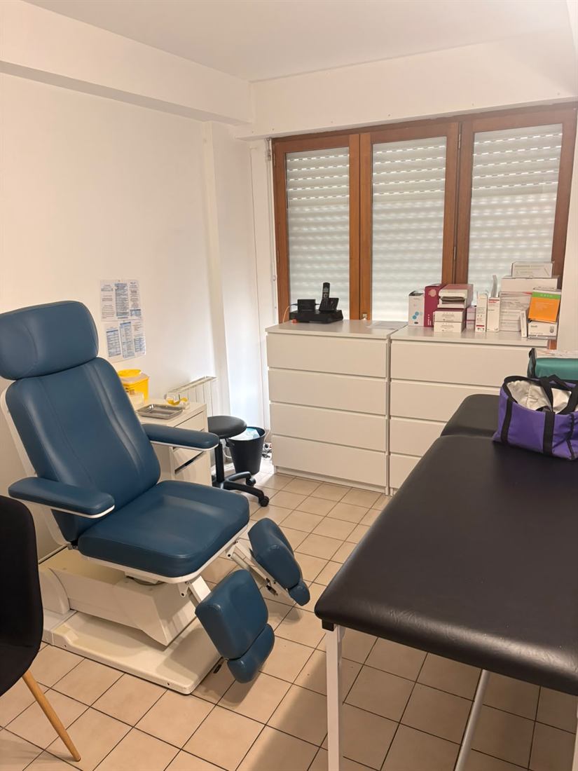 Fauteuil de prélèvement bleu à côté d'une table d'examen et des rangements du matériel.
