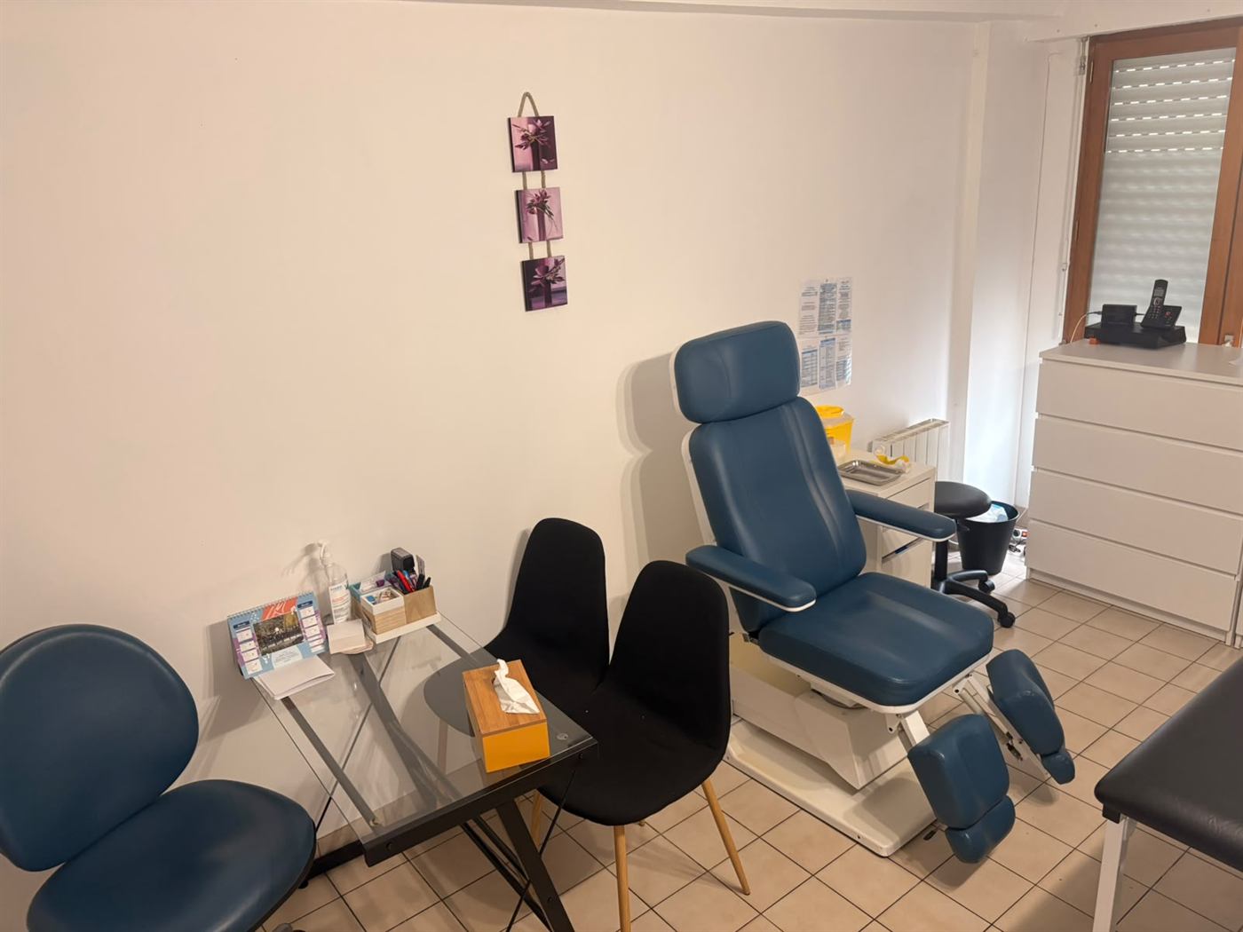 Salle de soins : fauteuil de prélèvement bleu, bureau en verre et collecteur à aiguilles.